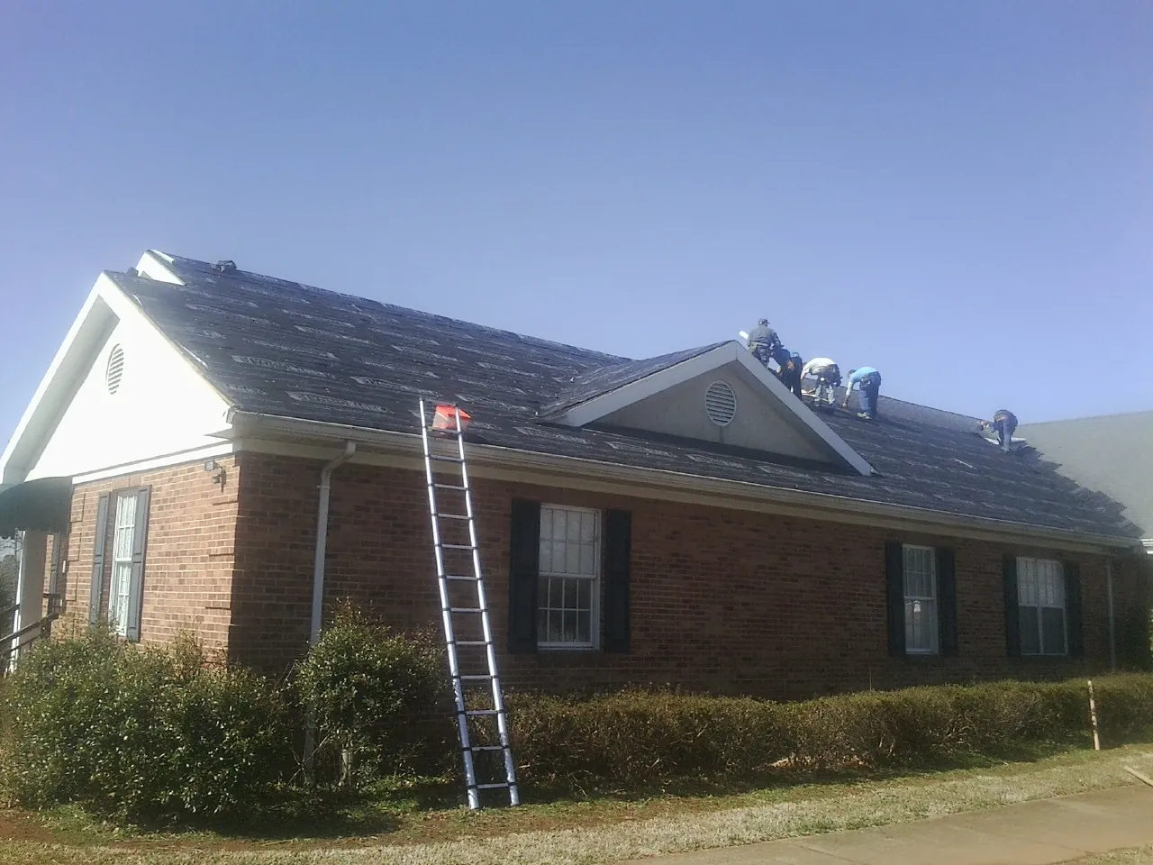 Crew tearing shingles off a brick ranch roof with a ladder set — Emergency Roof Repair work by our crew in Talmo