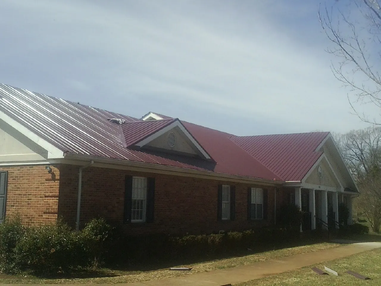 Red metal roof with gabled entries on a long brick building, from a Hail Damage Roof Repair job in Talmo