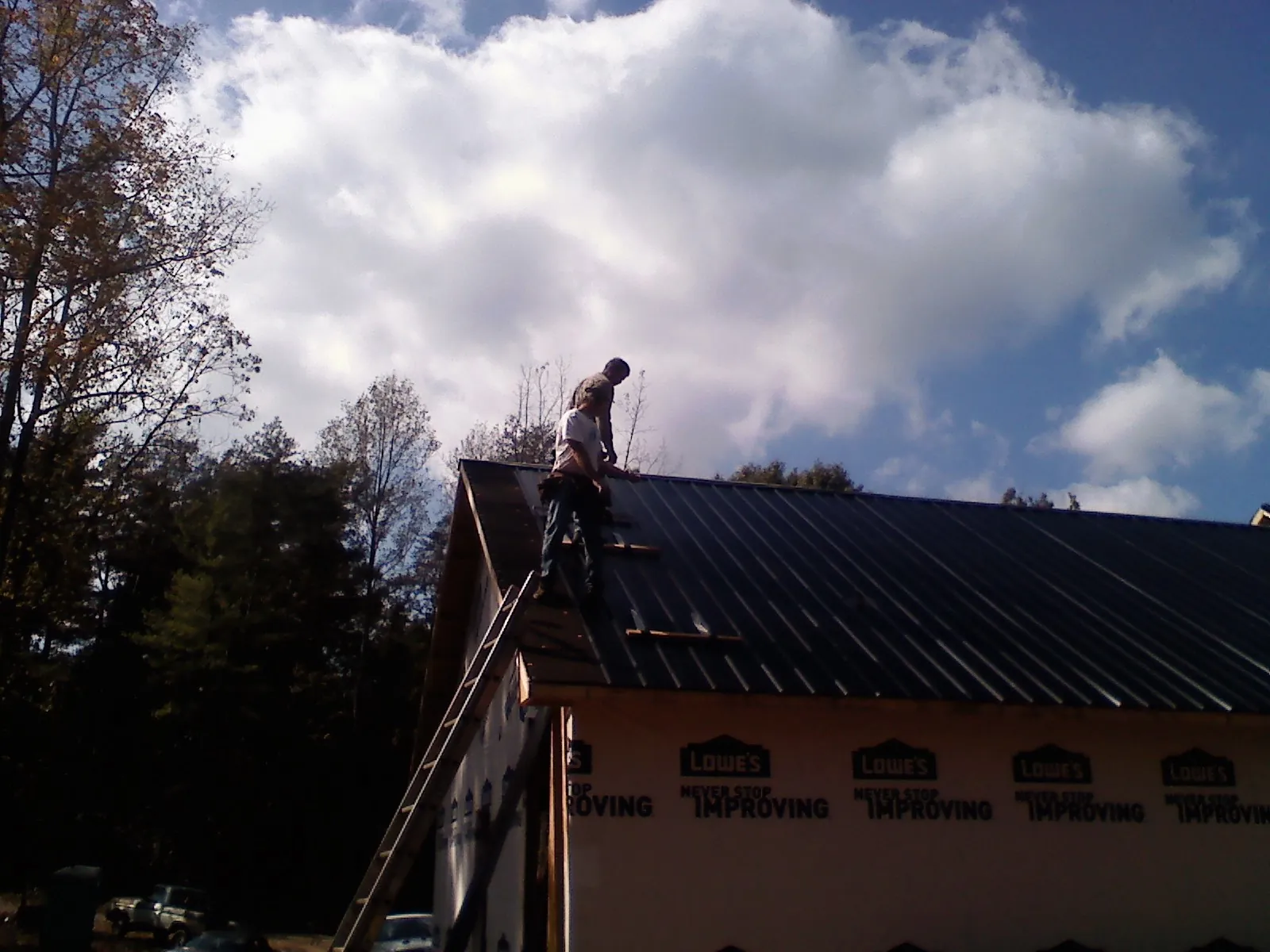 Roofer fastening dark metal panels high against a cloudy sky, from a Roof Inspection job in Talmo