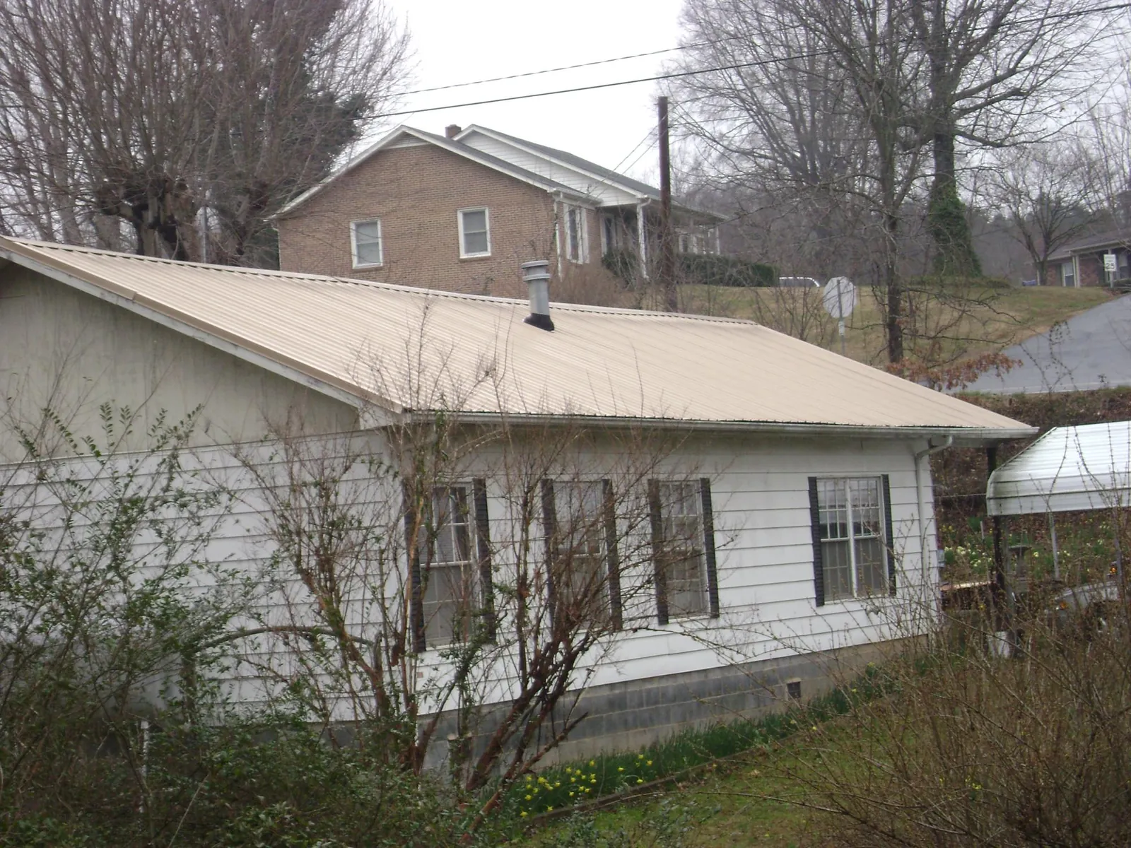 Tan metal roof on a white sided house set into a hillside — Commercial Roofing by Roofing Brothers in Talmo