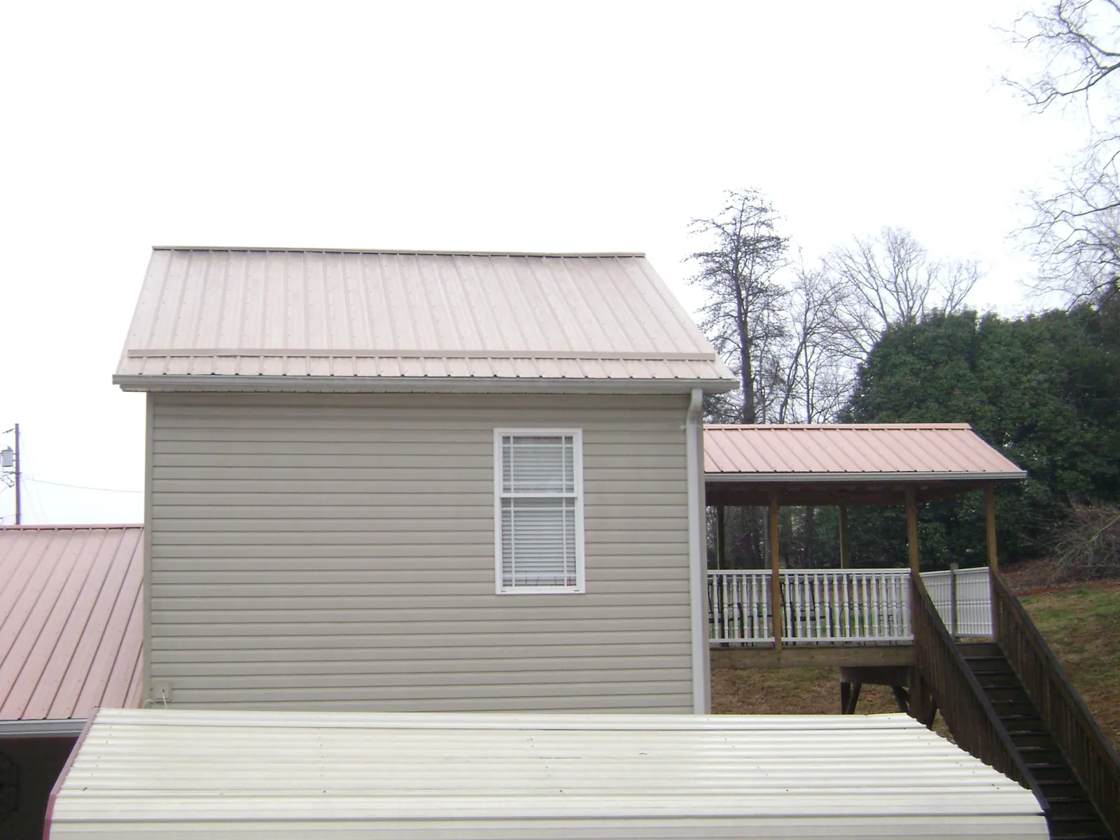 Tan metal roofs on a two story addition and attached porch, from a Roof Replacement job in Talmo